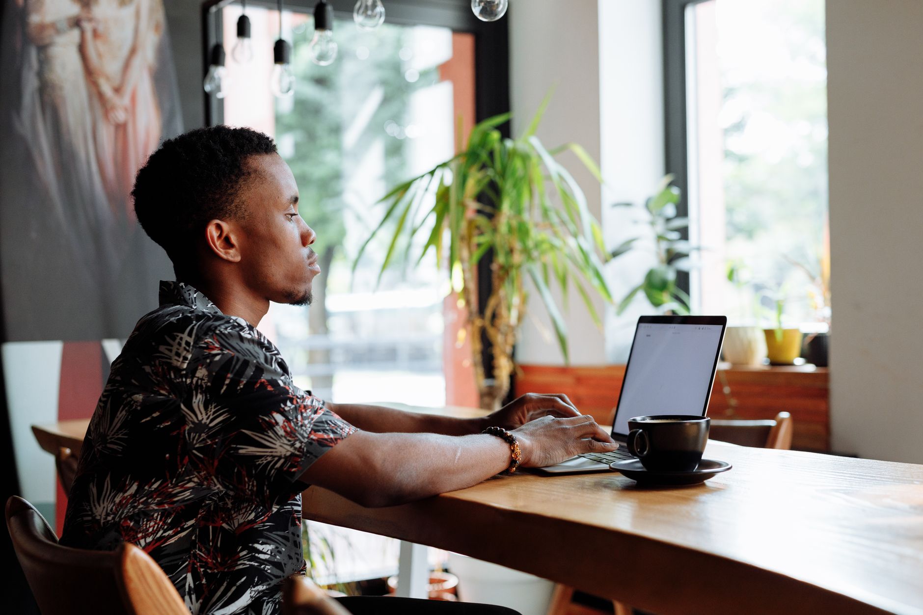 Side view of a person typing on a laptop at a busy cafe while another person sits nearby