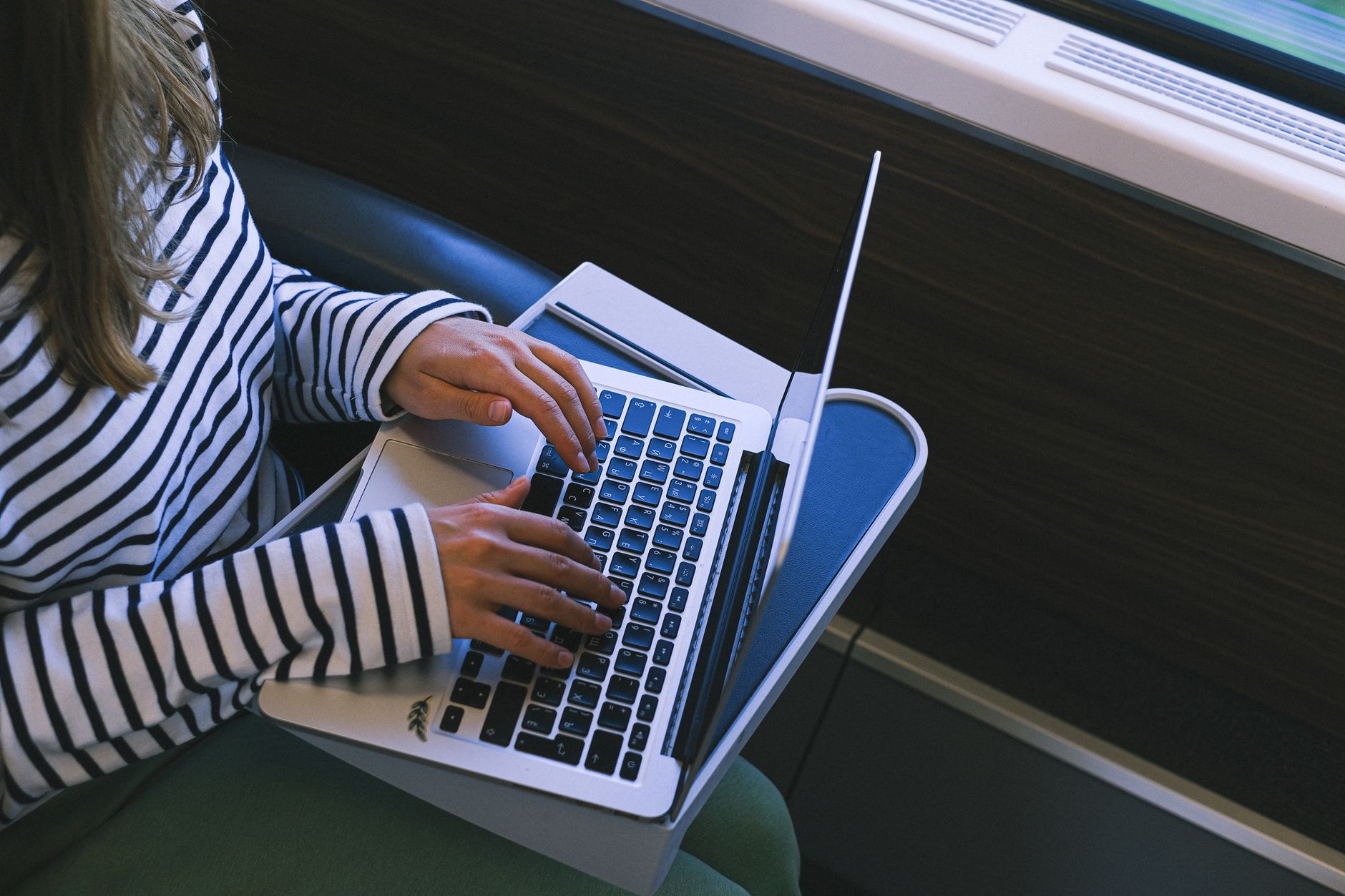 A person using a laptop with a privacy screen attached while sitting on a train with other passengers nearby.