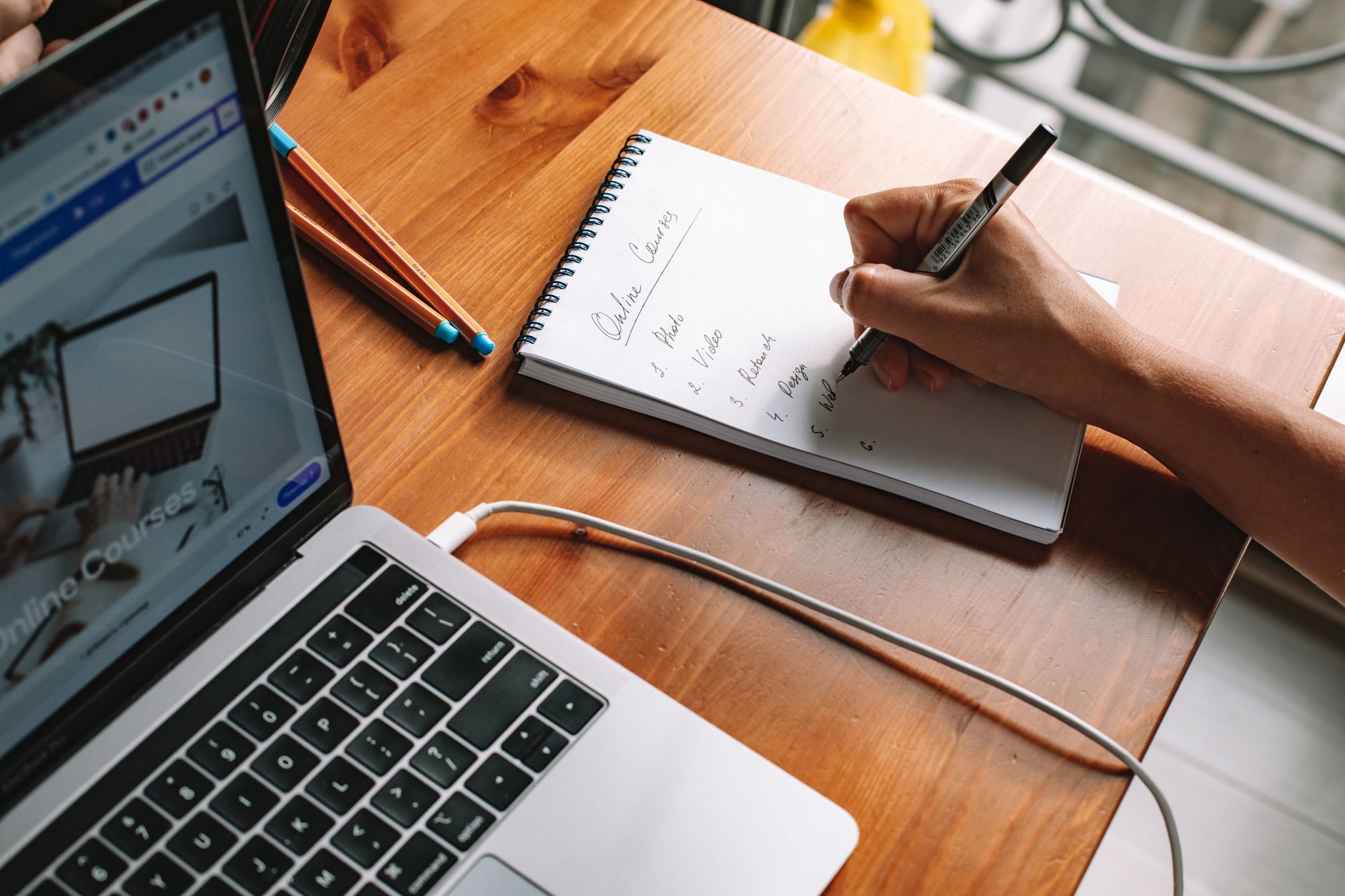 Person holding a printed list of websites while sitting at a kitchen table with a laptop open.