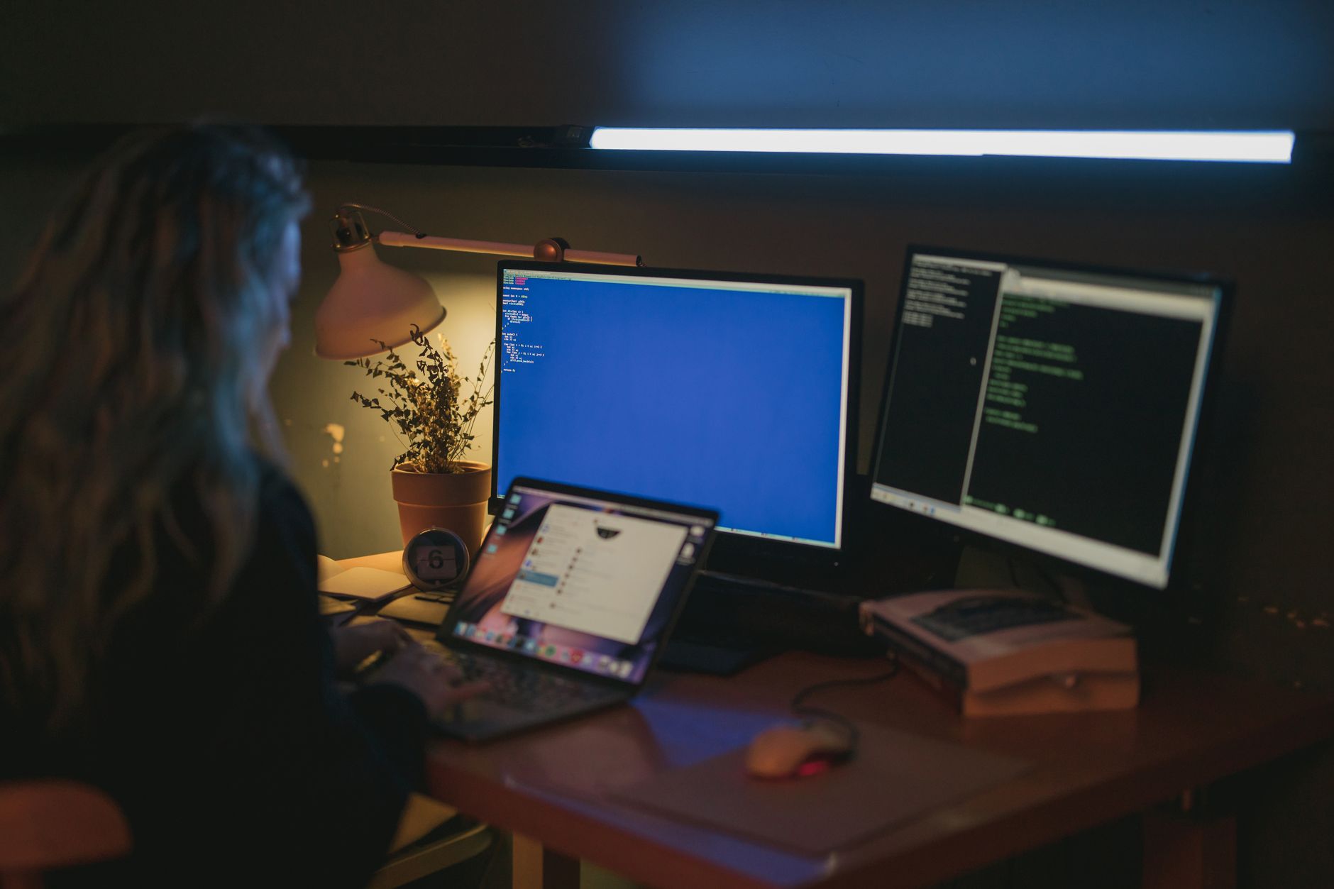 A person sitting alone at a home desk at night, face lit by the glow of an open laptop screen